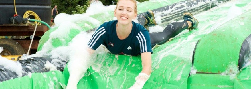 Picture of a female runner sliding down a water slide head first as part of a muddy run race
